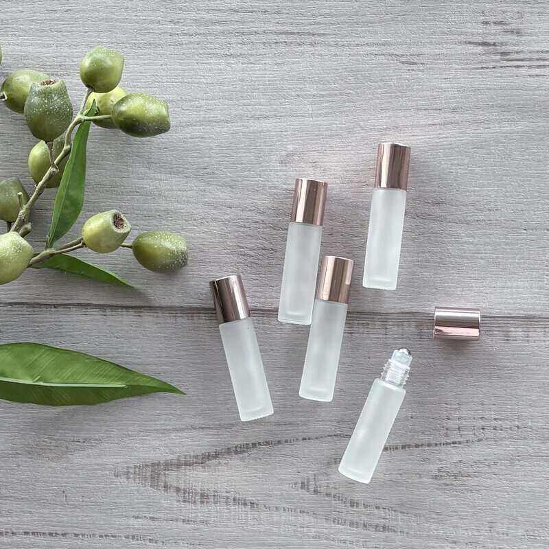 Set of clear glass bottles with rose gold caps on a wooden surface with green leaves.