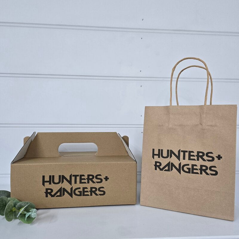Two brown kraft paper packaging bags with black printed 'HUNTERS+RANGERS' branding, displayed on a white surface against a white paneled wall.