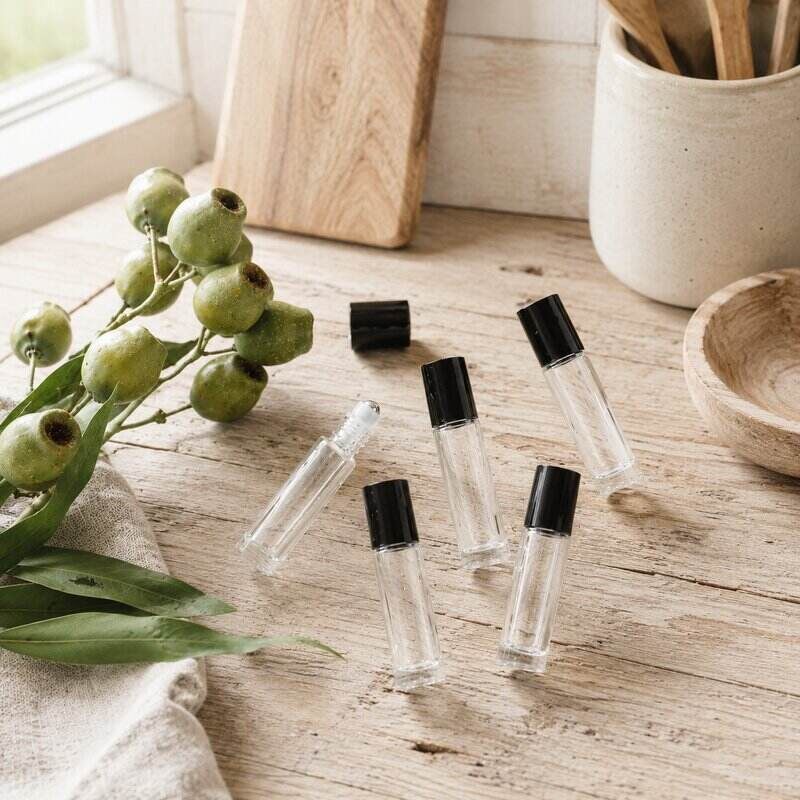 Clear rollerball bottles with black caps on a wooden surface with greenery and a window in the background.