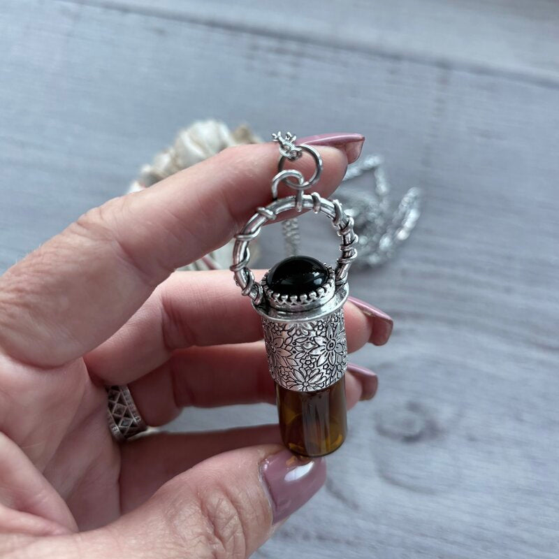Amber glass roller with ornate silver lid with black onyx crystal stone & silver chain necklace pictured held in hand with sage smudge stick in background