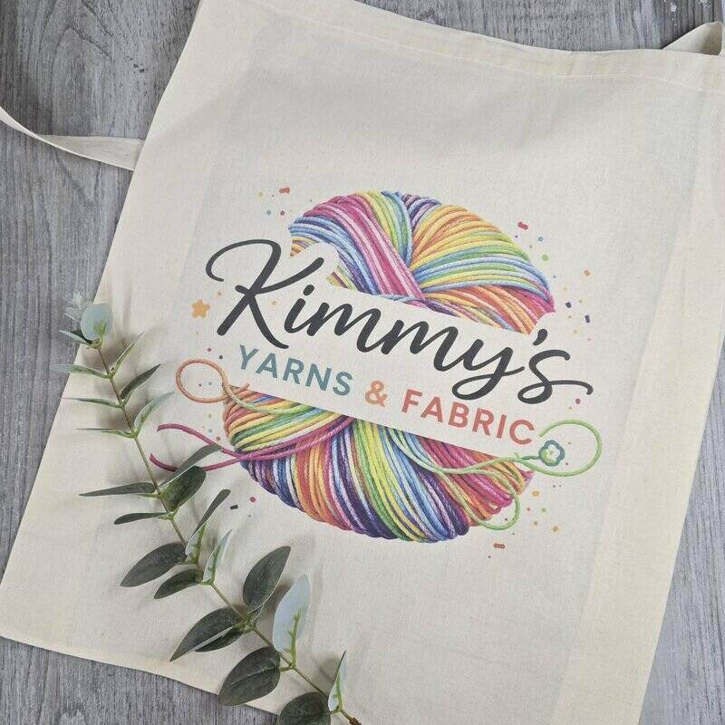 Tote bag with 'Kimmy's Yarns & Fabric' logo featuring colorful yarn balls on a wooden surface.