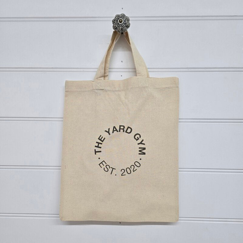 Beige tote bag with 'The Yard Gym' logo on a white background