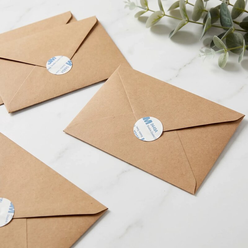 Three brown envelopes with round stickers on a light surface with a plant in the corner.