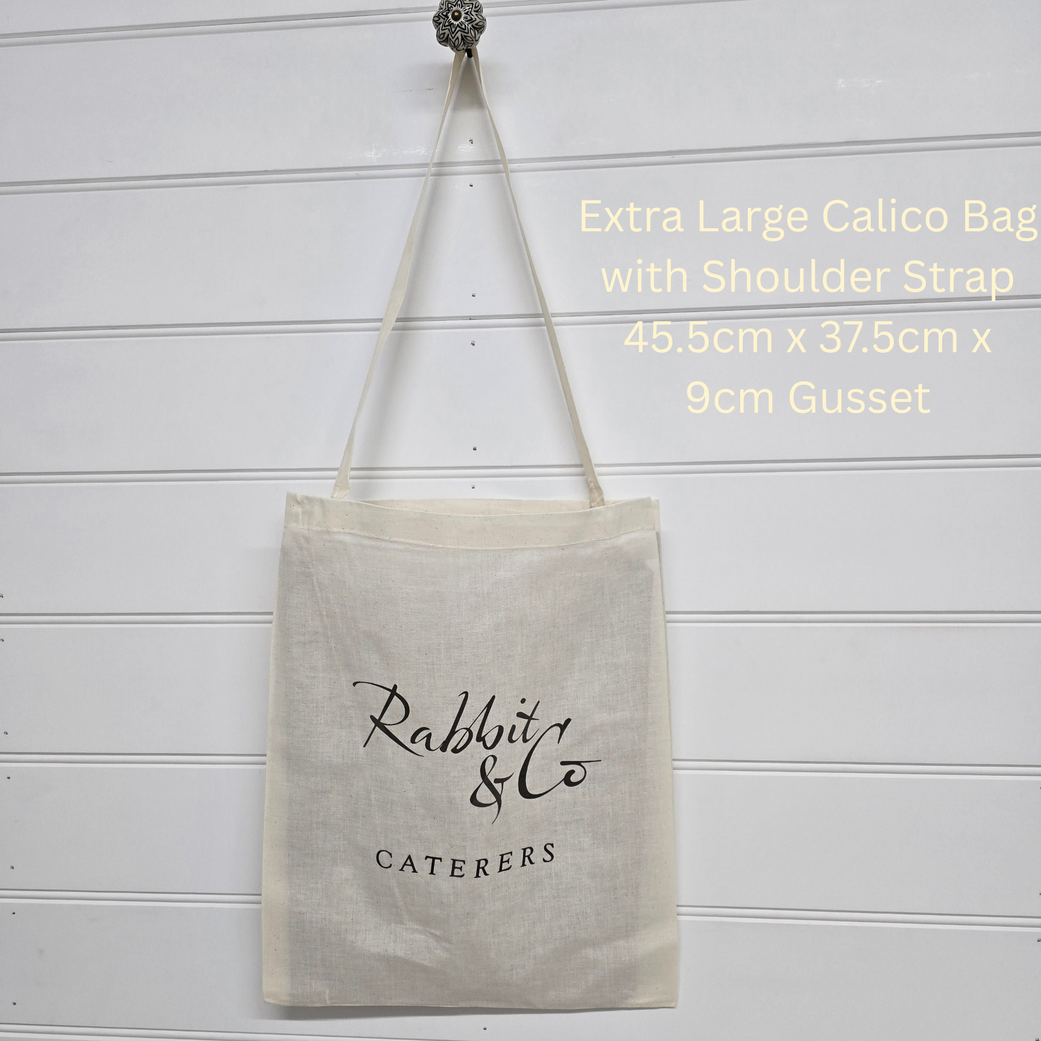 Beige tote bag with 'Rabbit & Co Caterers' branding on a white wooden background