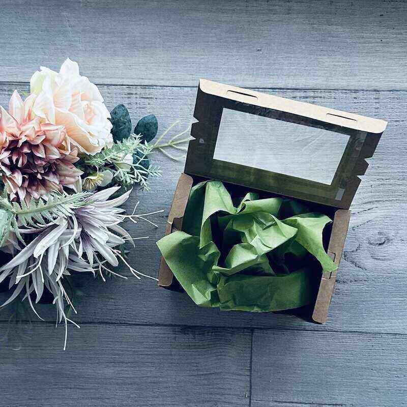 Open cardboard box with green tissue paper next to a bouquet of flowers on a wooden surface