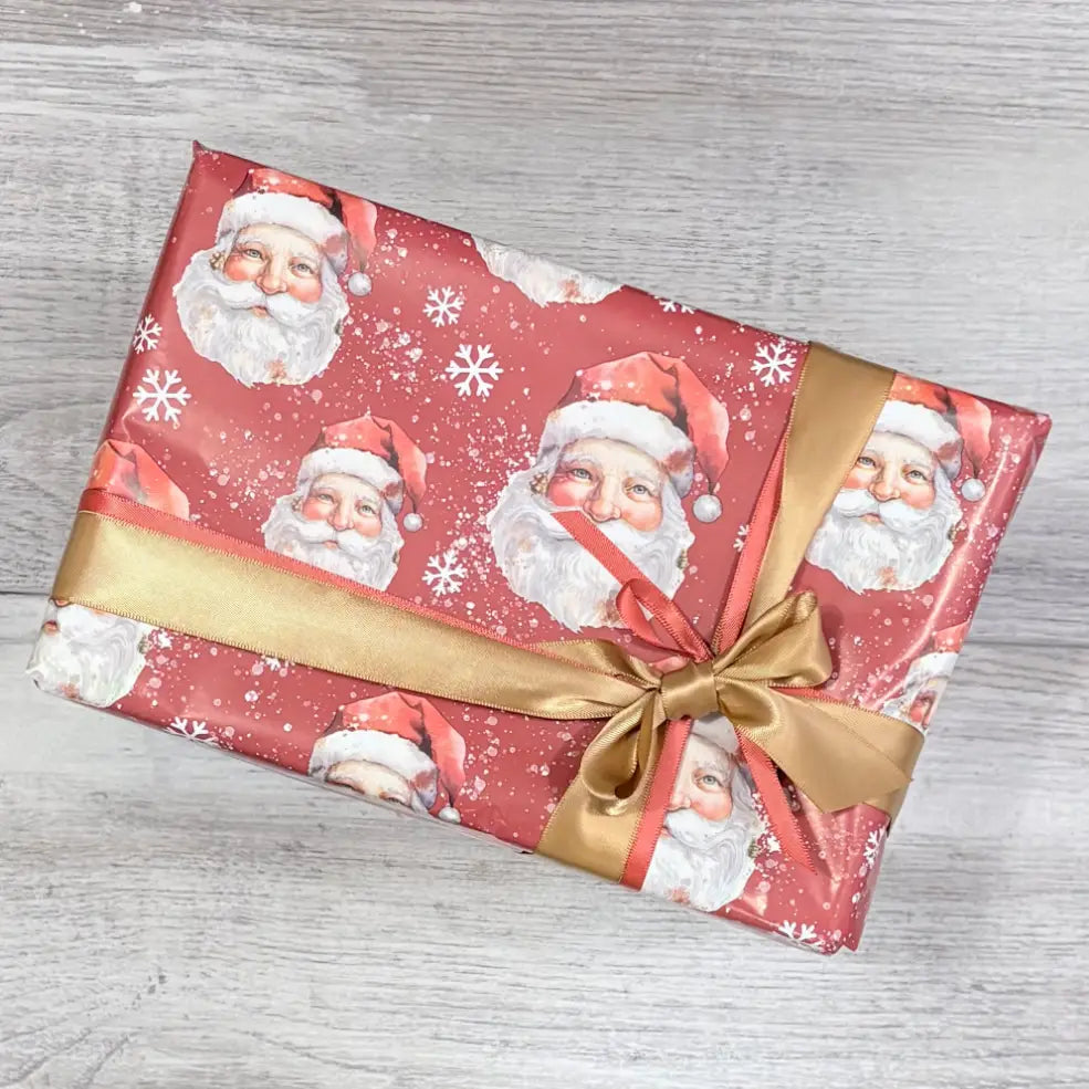 box wrapped in red santa face wrapping paper with gold and rust satin ribbon