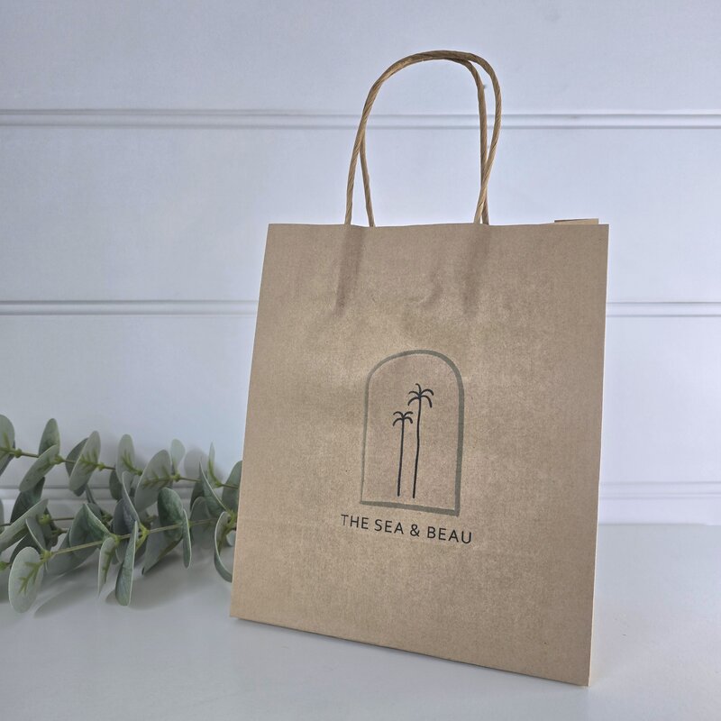 Brown paper bag with 'The Sea & Beau' logo on a white background