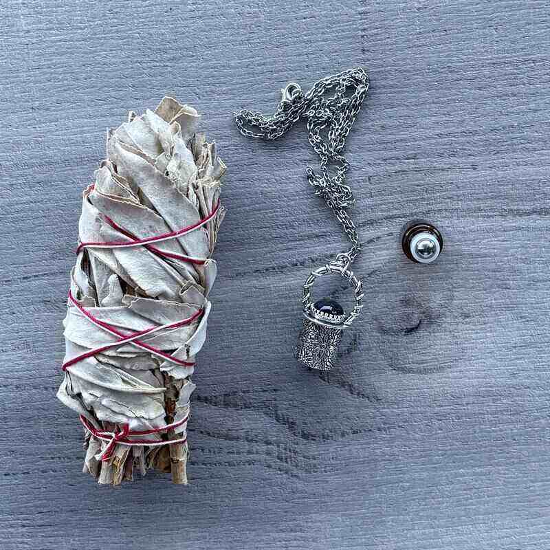 Amber glass roller with ornate silver lid with amethyst crystal stone & silver chain necklace next to roller pictured with sage smudge stick