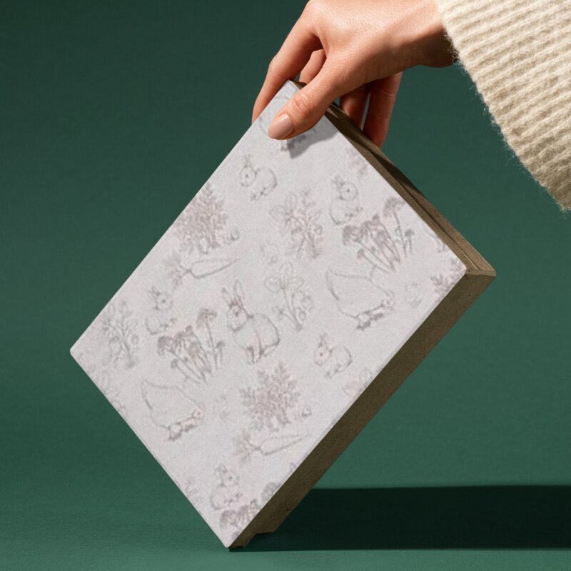Hand holding a notebook with embossed illustrations on a green background