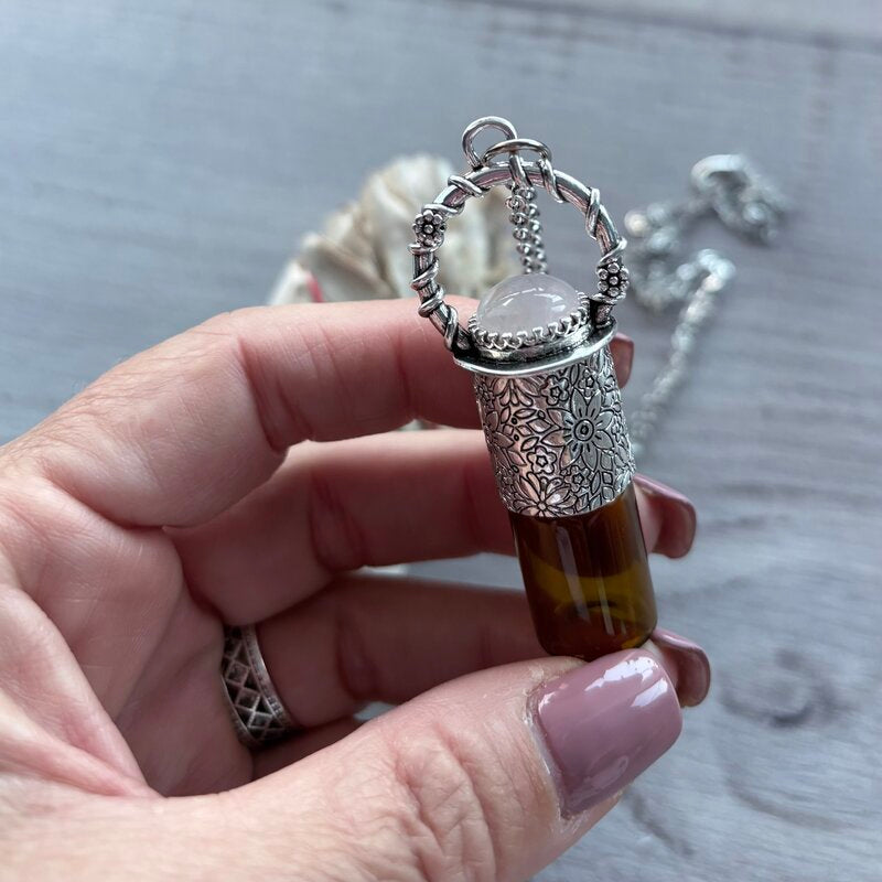 Amber glass roller with ornate silver lid with rose quartz crystal stone & silver chain necklace pictured held in hand with sage smudge stick in background